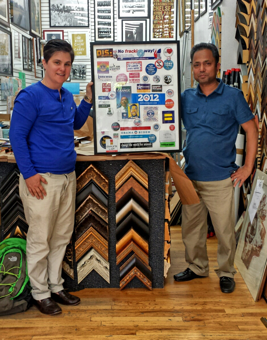 The Westside Frame Shop team holding a custom-framed collage beside a rack of moulding samples